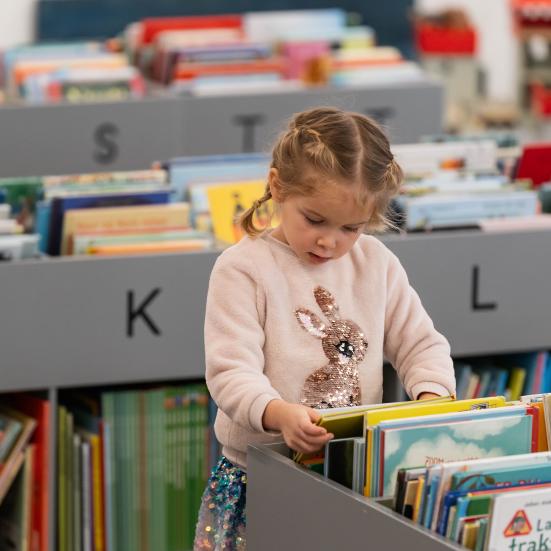 Lille pige kigger på billedbøger på biblioteket